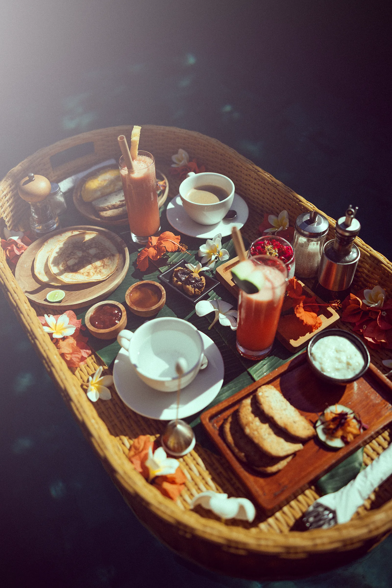 A floating breakfast on a rattan tray in the pool, with tropical fruit, fresh juice and frangipani petals