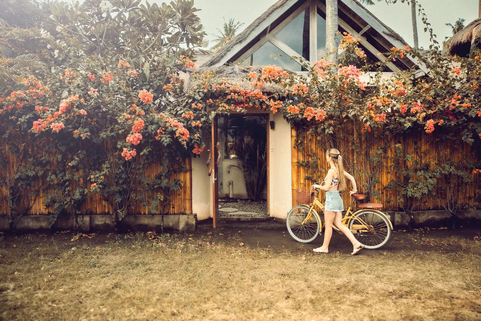 A guest walks a bicycle past a palm-roofed villa on traffic-free Gili Air