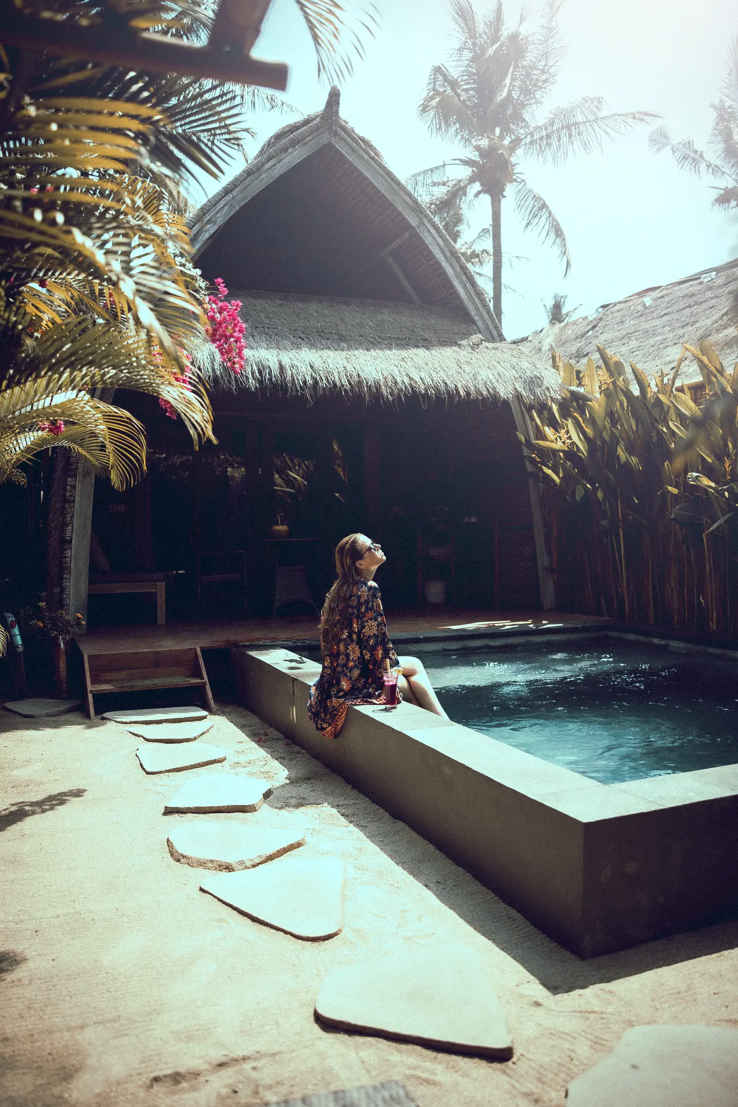 A guest sitting by the private plunge pool of a Lumbung villa at Anahata, the palm-roofed villa behind