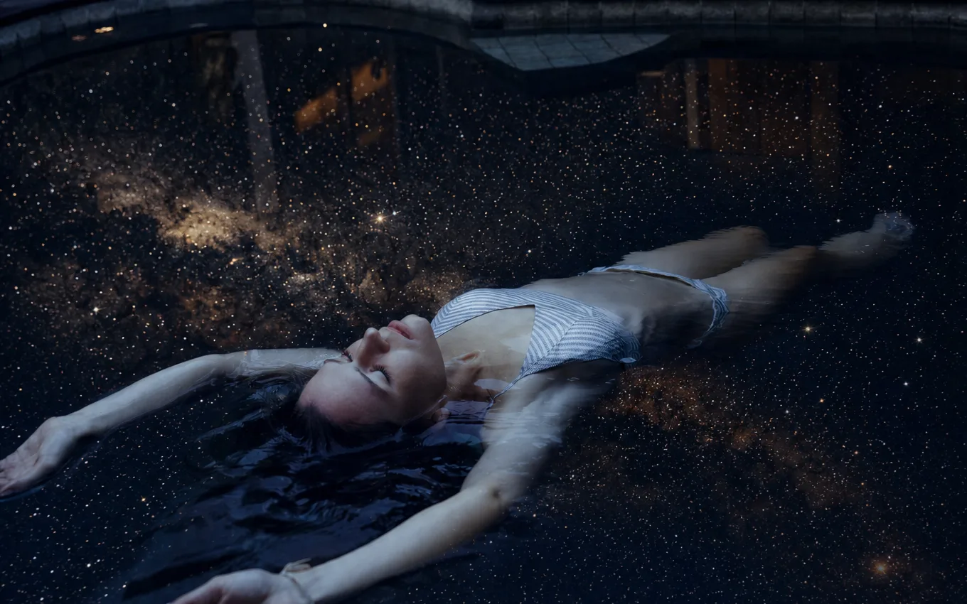 A guest floating in Anahata's private pool at night, the water mirroring a starry sky
